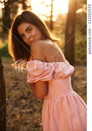 Looking in the camera. Pretty young woman in pink dress is in the forest 133262839