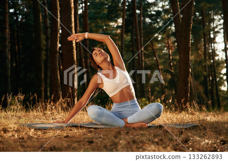 Many of the trees at background, sitting. Woman is doing yoga fitness exercises in the forest Many of the trees at background, sitting. Woman is doing yoga fitness exercises in the forest 133262893