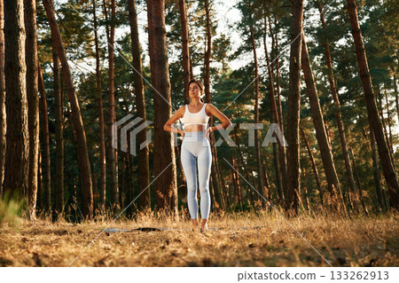 Confident facial expression. Woman is doing yoga fitness exercises in the forest 133262913