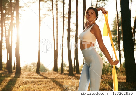 Yellow stretching band in hands. Woman is doing yoga fitness exercises in the forest Yellow stretching band in hands. Woman is doing yoga fitness exercises in the forest 133262950