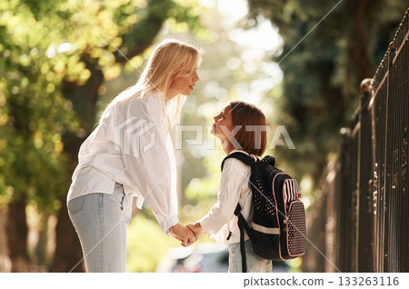 Holding the hands. Schoolgirl with her mother are outdoors together 133263116