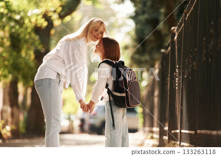 Holding the hands. Schoolgirl with her mother are outdoors together Holding the hands. Schoolgirl with her mother are outdoors together 133263118