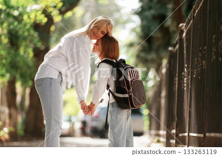 Woman is supporting daughter. Schoolgirl with her mother are outdoors together Woman is supporting daughter. Schoolgirl with her mother are outdoors together 133263119