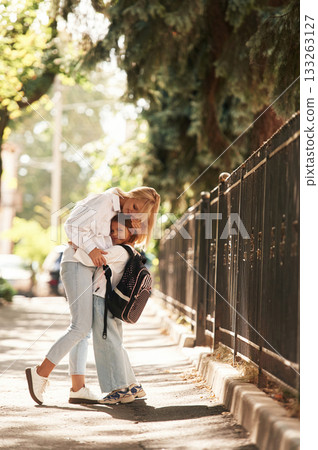 Embracing each other. Schoolgirl with her mother are outdoors together 133263127