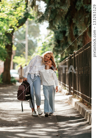 Schoolgirl with her mother are outdoors together Schoolgirl with her mother are outdoors together 133263129