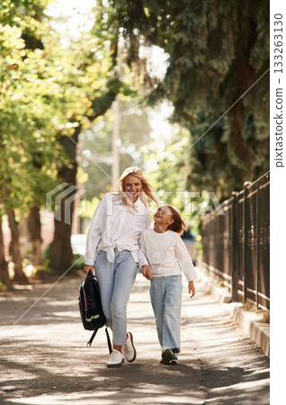 Holding the hands. Schoolgirl with her mother are outdoors together Holding the hands. Schoolgirl with her mother are outdoors together 133263130