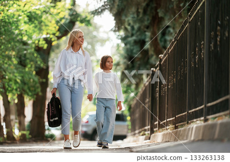 Leading the daughter to school. Little girl with her mother are outdoors together Leading the daughter to school. Little girl with her mother are outdoors together 133263138
