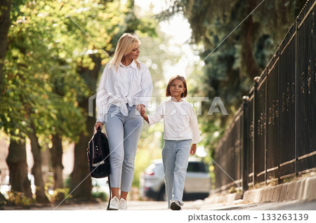 Leading the daughter to school. Little girl with her mother are outdoors together Leading the daughter to school. Little girl with her mother are outdoors together 133263139