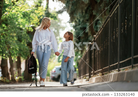 Leading the daughter to school. Little girl with her mother are outdoors together Leading the daughter to school. Little girl with her mother are outdoors together 133263140
