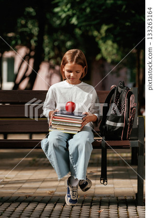 An apple on the books. Schoolgirl is sitting on the bench outdoors An apple on the books. Schoolgirl is sitting on the bench outdoors 133263164