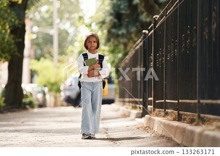 Holding notepad. Schoolgirl with backpack is outdoors Holding notepad. Schoolgirl with backpack is outdoors 133263171