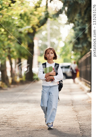 Holding notepad. Schoolgirl with backpack is outdoors 133263176