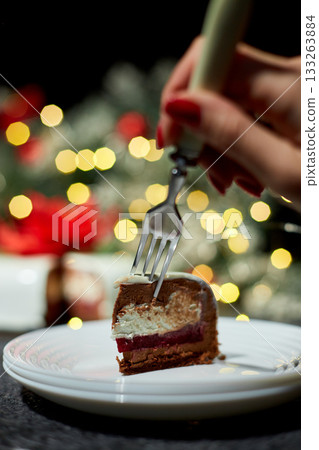 A Hand Reaching for a Slice of Decadent Layered Dessert on a Festive Table Decorated With Twinkling Lights During the Holiday Season A Hand Reaching for a Slice of Decadent Layered Dessert on a Festive Table Decorated With Twinkling Lights During the Holiday Season 133263884