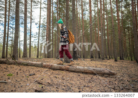 Smiling woman on fallen tree trunk in woods. Playful hiker balancing in quiet forest alone 133264007