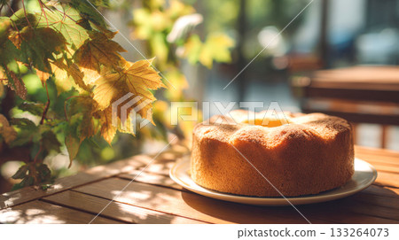 Simple, beautifully baked bundt or chiffon cake on a wooden outdoor patio table, highlighted by warm autumn sunlight and golden leaves. Represents cozy fall baking, dessert, and cafe moments 133264073
