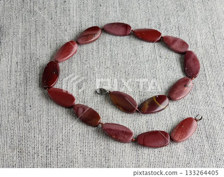 Natural stone, irregularly shaped red jasper beads on a burlap background 133264405