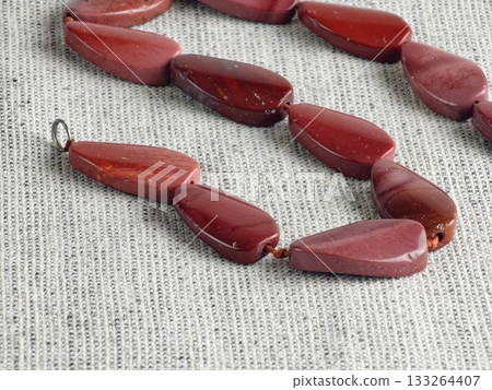Natural stone, irregularly shaped red jasper beads on a burlap background. Close-up Natural stone, irregularly shaped red jasper beads on a burlap background. Close-up 133264407