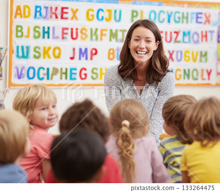 Smiling Female Teacher with a Group of Happy Preschool or Kindergarten Children Sitting Together in a Classroom During a Lesson, Focused on Education and Early Learning 133264475
