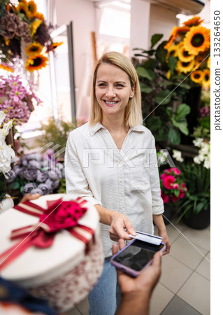 Woman paying with NFC technology on smartphone in flower shop Woman paying with NFC technology on smartphone in flower shop 133264650