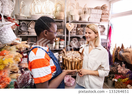 Shop assistant showing wicker basket to customer in a flower shop Shop assistant showing wicker basket to customer in a flower shop 133264651