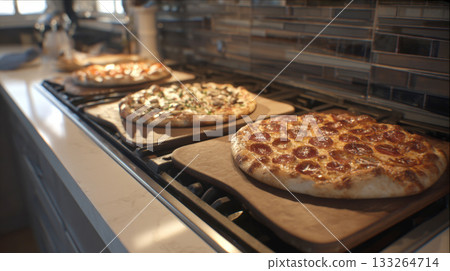 A row of three freshly baked pizzas on wooden peels resting on a kitchen stovetop. The pizzas include pepperoni and mushroom, highlighting a family meal, home cooking, delicious variety of pizza night 133264714