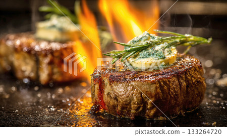 two thick-cut filet mignon steaks being seared on a hot surface, topped with melting herb butter and rosemary. Dramatic flames and steam rise around the gourmet meat, showcasing a professional cooking 133264720
