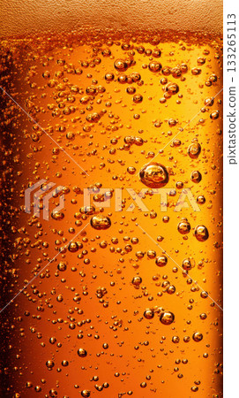 glass filled with a deep amber-colored, carbonated beverage, showcasing countless golden bubbles rising, forming foam at top. Themes of refreshment, movement, crispness of drinks beer 133265113