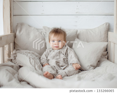 baby sitting in a natural light setting with wooden paneling and neutral linens. The image conveys a sense of peaceful home life, natural materials, comfort, sweet innocence of early childhood 133266065