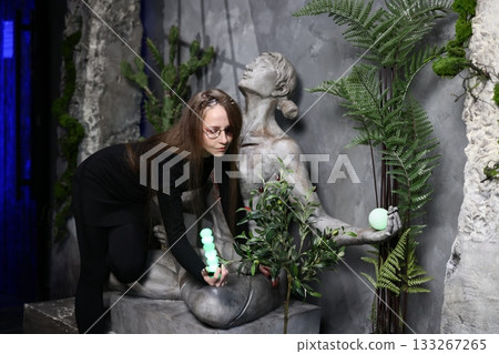 Woman carefully arranging greenery around statue during sunset ambiance 133267265