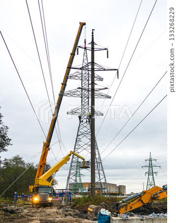 Workers installing high-voltage power line tower using cranes and heavy machinery in Latvia 133268229