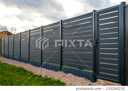 Modern dark gray metal privacy fence with gate installed along residential property boundary Modern dark gray metal privacy fence with gate installed along residential property boundary 133268232