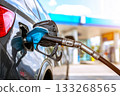 A car is refueling at a outdoors gas station in an urban setting. A close-up of the fuel pump being inserted into the tank. Gas pump nozzles 133268565