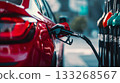 A car is refueling at a outdoors gas station in an urban setting. A close-up of the fuel pump being inserted into the tank. Gas pump nozzles 133268567