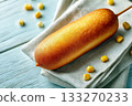 Classic golden-brown corndog on a stick served on a folded cloth napkin with scattered corn kernels on a blue wooden surface 133270233