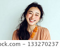 Smiling young woman holding a skewer of dried candied fruit against a light background, wearing peach-colored clothing 133270237