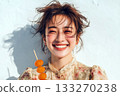 Cheerful young woman with tousled hair holding a skewer of candied fruit and laughing in the sunlight against a light wall 133270238
