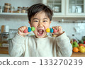 Excited young boy holding two colorful candy skewers and smiling widely in a bright home kitchen setting 133270239