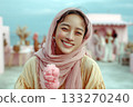 Smiling young woman in a pink hijab holding a pink ice cream cone at an outdoor pastel-themed gathering 133270240
