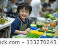 Smiling young boy in green overalls enjoying colorful jelly treats at a lively kitchen table filled with snacks and ingredients 133270243