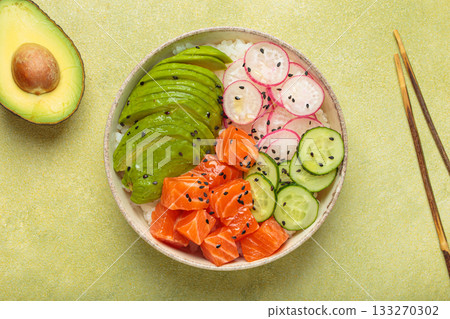 Salmon poke bowl with avocado, radish, cucumber and rice on green background top view 133270302