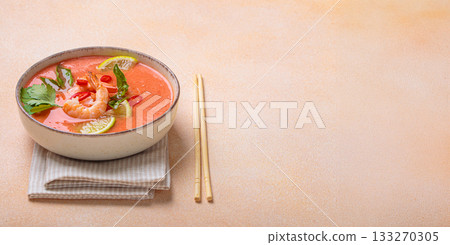 Traditional Thai soup tom yum soup with shrimp, lime, and herbs in bowl with chopsticks on light beige background, space for text 133270305