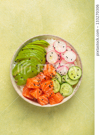 Salmon poke bowl with avocado, radish, cucumber and rice on green background top view 133270306