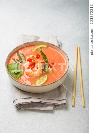 Traditional Thai soup tom yum soup with shrimp, lime, and herbs in bowl with chopsticks on light grey background 133270318
