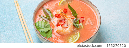 Traditional Thai soup tom yum soup with shrimp, lime, and herbs in bowl with chopsticks on blue background 133270320