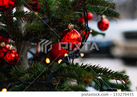 Red Christmas balls and garlands on branch. Christmas tree with decor. Holiday season, street decorations. 133270435