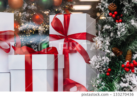 Gift boxes in store window. Season of Christmas shopping and sales. White boxes with red ribbons on background of Christmas decorations. 133270436