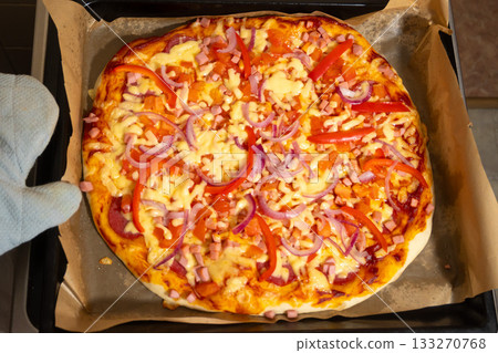 Ready Pizza with Cheese and Vegetables Taken Out of Oven in Mitt 133270768