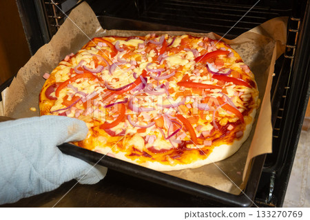 Homemade Pizza with Vegetables and Ham Baking in Oven on Parchment 133270769