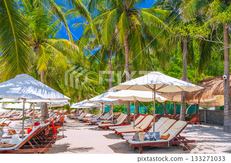 sun umbrellas and beds on sandy beach under palm trees at a luxury seaside resort in summer. Beach by sea on tropical exotic island in Asia. Tourist holidays and travel 133271033