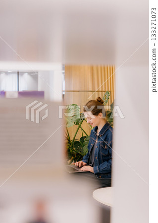 young woman is sitting and working on laptop against background of green monstera. young woman is sitting and working on laptop against background of green monstera. 133271073